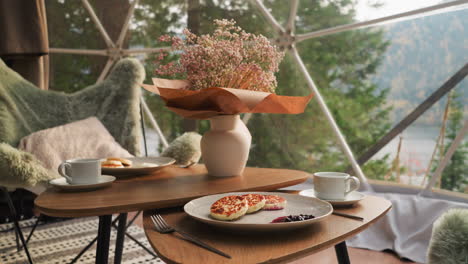 vase with autumn flowers on served low table. coffee table paired with cozy armchairs creates perfect spot to enjoy breakfast against breathtaking views of lake