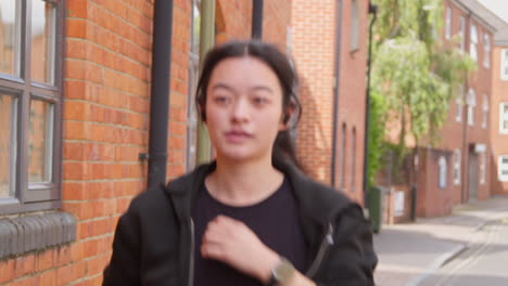 무선 이어폰을 착용한 젊은 여성이 도시 거리를 따라 달리기를 연습하고 있습니다.
