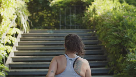 vista trasera de una mujer caucásica gordo corriendo por las escaleras en el parque