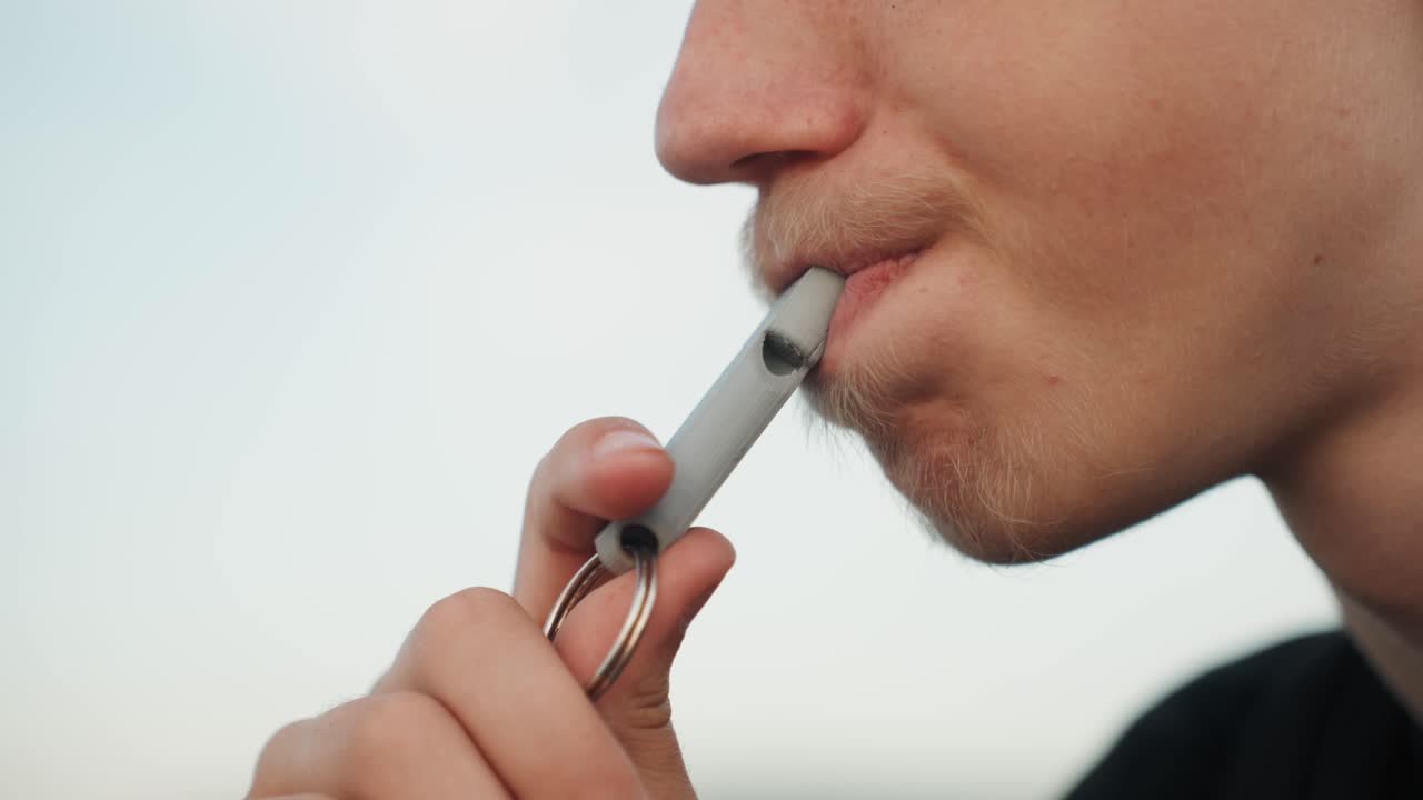 Primo piano di uno studente caucasico che svapa all'aperto. Vista di profilo di un giovane uomo che utilizza un vaporizzatore portatile attaccato a un portachiavi, con una leggera barba. Il dispositivo metallico è tenuto tra le dita, in un'atmosfera calma e riflessiva, sotto una morbida luce serale.