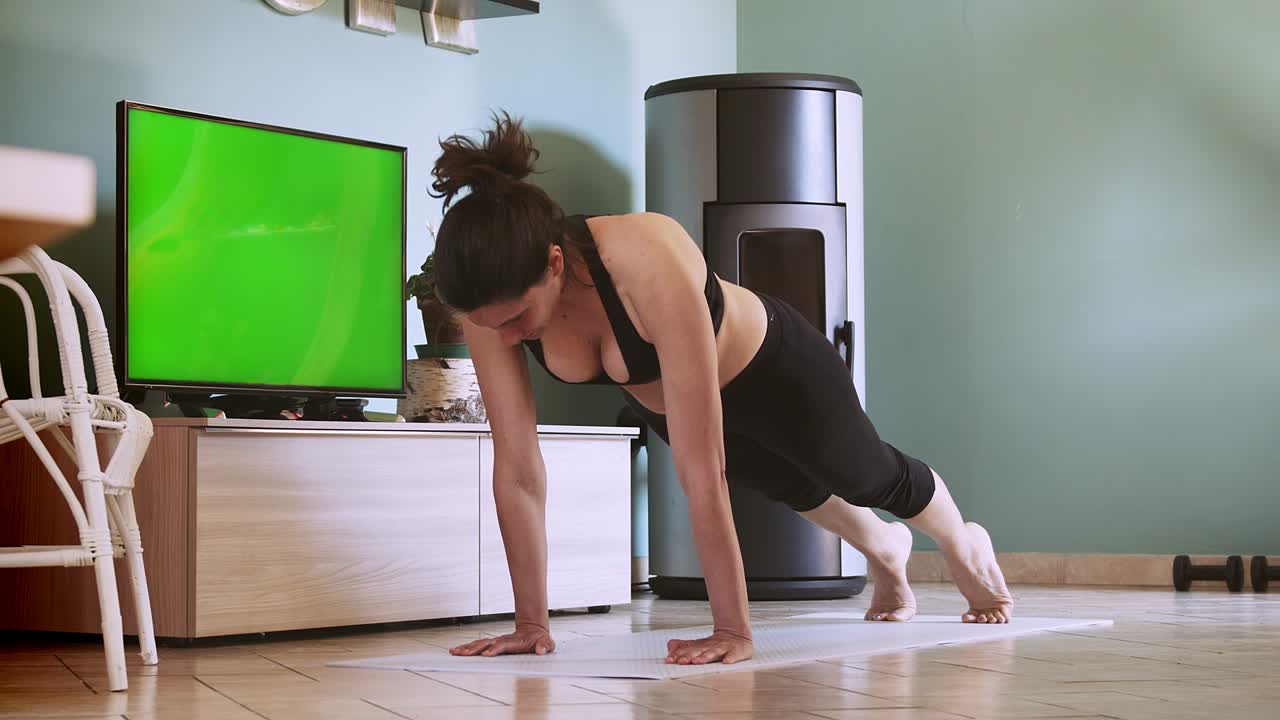 mujer haciendo ejercicio en casa después de una clase de fitness remota. mujer haciendo entrenamiento en casa con televisión de pantalla verde. entrenamiento de abdominales de tabla. transmisión de entrenamiento doméstico de pantalla verde