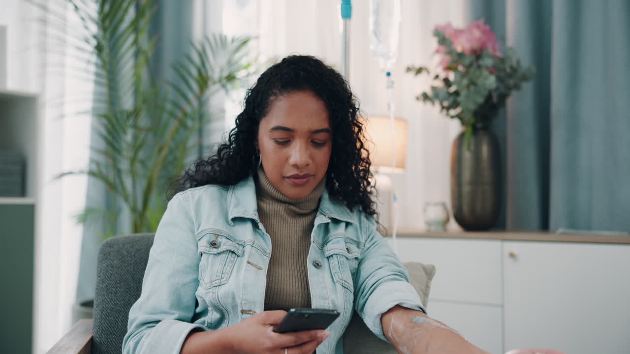 Woman sitting in a chair at home with an IV, smiling and using her phone