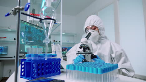 scienziato in tuta protettiva che conduce l'analisi del virus utilizzando il microscopio