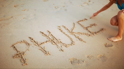 a female tourist writing phuket in the sand