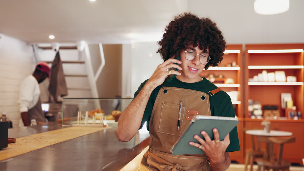 Waiter in a cafe talking on the phone while using a tablet