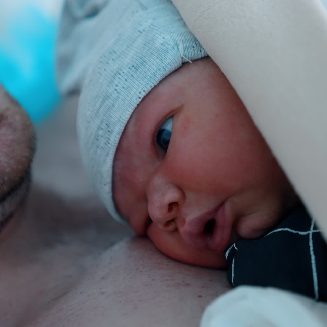 Newborn child looking shocked right after birth. Baby lies on dad's chest covered with blanket