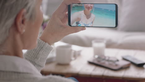 Mujer-Madura-Teniendo-Video-Chat-Usando-Un-Teléfono-Inteligente-Saludando-A-Su-Hija-En-Una-Playa-De-Vacaciones-En-Italia-Compartiendo-Experiencias-De-Viaje-En-Un-Teléfono-Móvil-Disfrutando-De-La-Conexión-Charlando-Con-Su-Abuela-4k