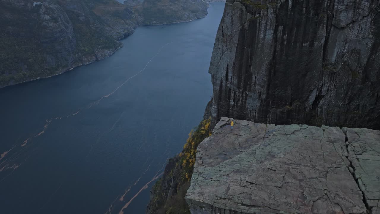 Person set fra høj vinkel på dramatisk klippelandskab, glødende i norsk solnedgang
