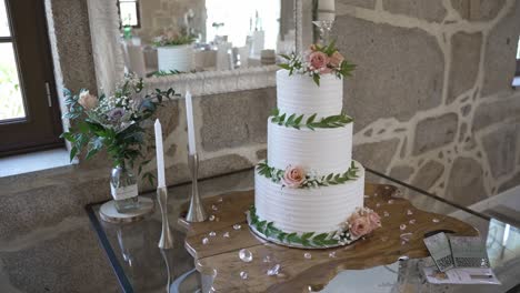 white wedding cake with greenery and peach roses on glass table