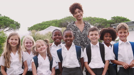 Outdoor-Portrait-Of-Elementary-School-Pupils-With-Teacher-Wearing-Uniform-Standing-On-Playing-Field