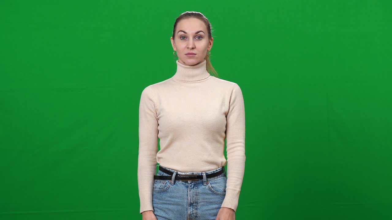 Seriøs, streng kvinde peger på kameraet, stående på grøn skærm. Portræt af krævende kaukasisk dame, der poserer foran en chromakey-baggrund og kigger ind i kameraet.