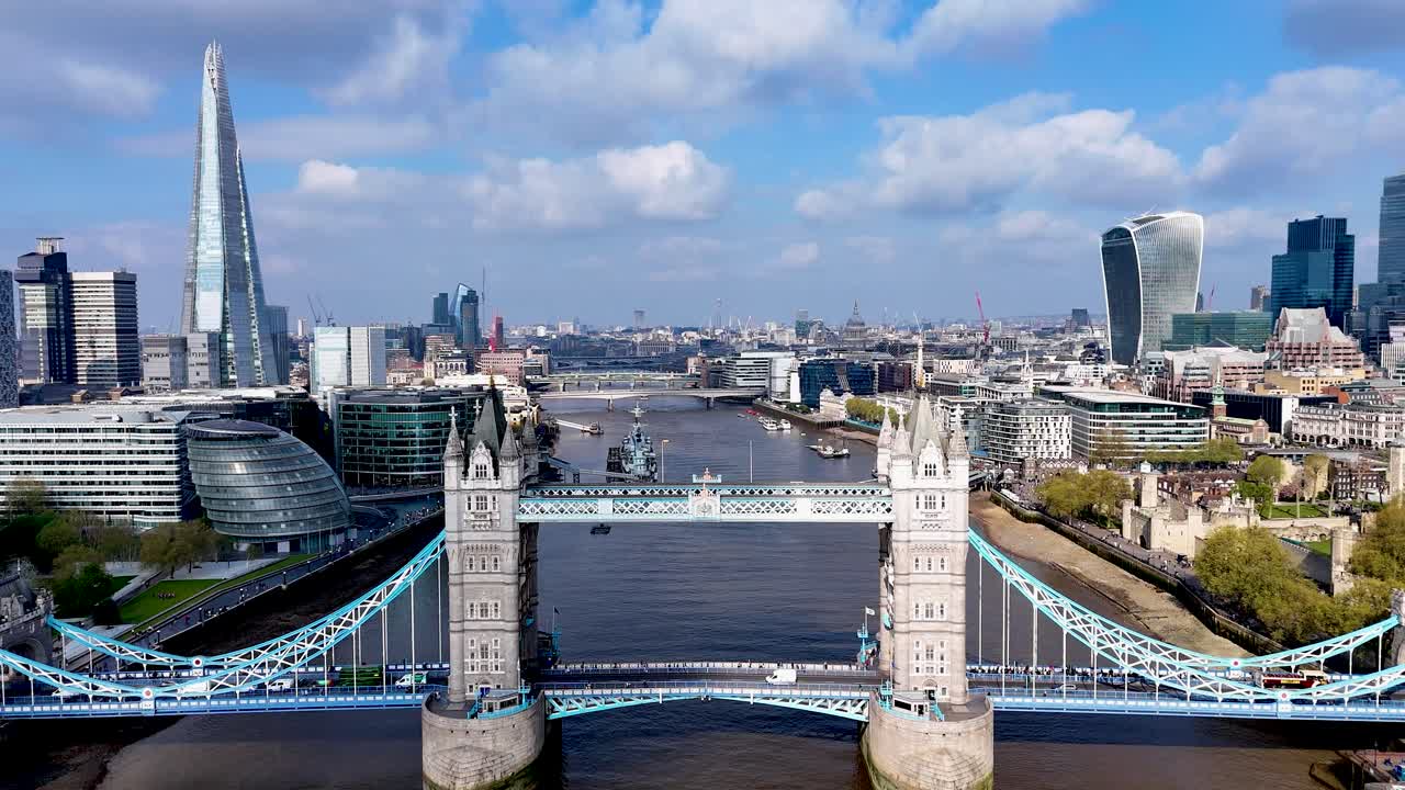 Aerial view approaching the City of London, soaring over the River Thames and London Bridge with dramatic blue skies and iconic skyscrapers in the distance.