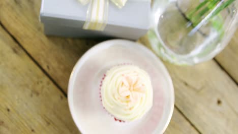 gift box and flower vase with cupcake in plate on wooden plank