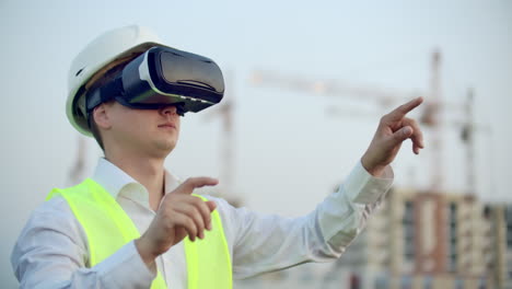 Porträt-Eines-Männlichen-Kranführers,-Der-Eine-Baustelle-Mithilfe-Einer-Virtual-Reality-Brille-Bedient.-Der-Bauleiter-Verwaltet-Den-Fortschritt-Und-Die-Planung-Von-Gebäuden-Mithilfe-Von-Gesten-Bei-Sonnenuntergang