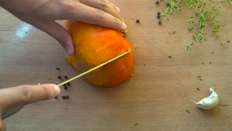 Top-down-view-of-male-hands-cutting-orange-pumpkin-in-slice-on-wooden-cutting-board