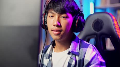 close up of asian teen boy gamer smiling to camera and showing thumb up while playing video game on computer