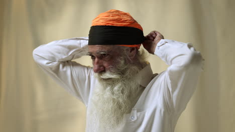 Fotografía-De-Estudio-De-Un-Hombre-Sikh-Mayor-Con-Barba-Atando-Tela-Para-Un-Turbante-Contra-Un-Fondo-Liso,-Filmada-En-Tiempo-Real