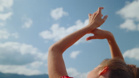mujer de primer plano manos cielo nublado. vista de atrás niña despreocupada levantando los brazos sobre la naturaleza.