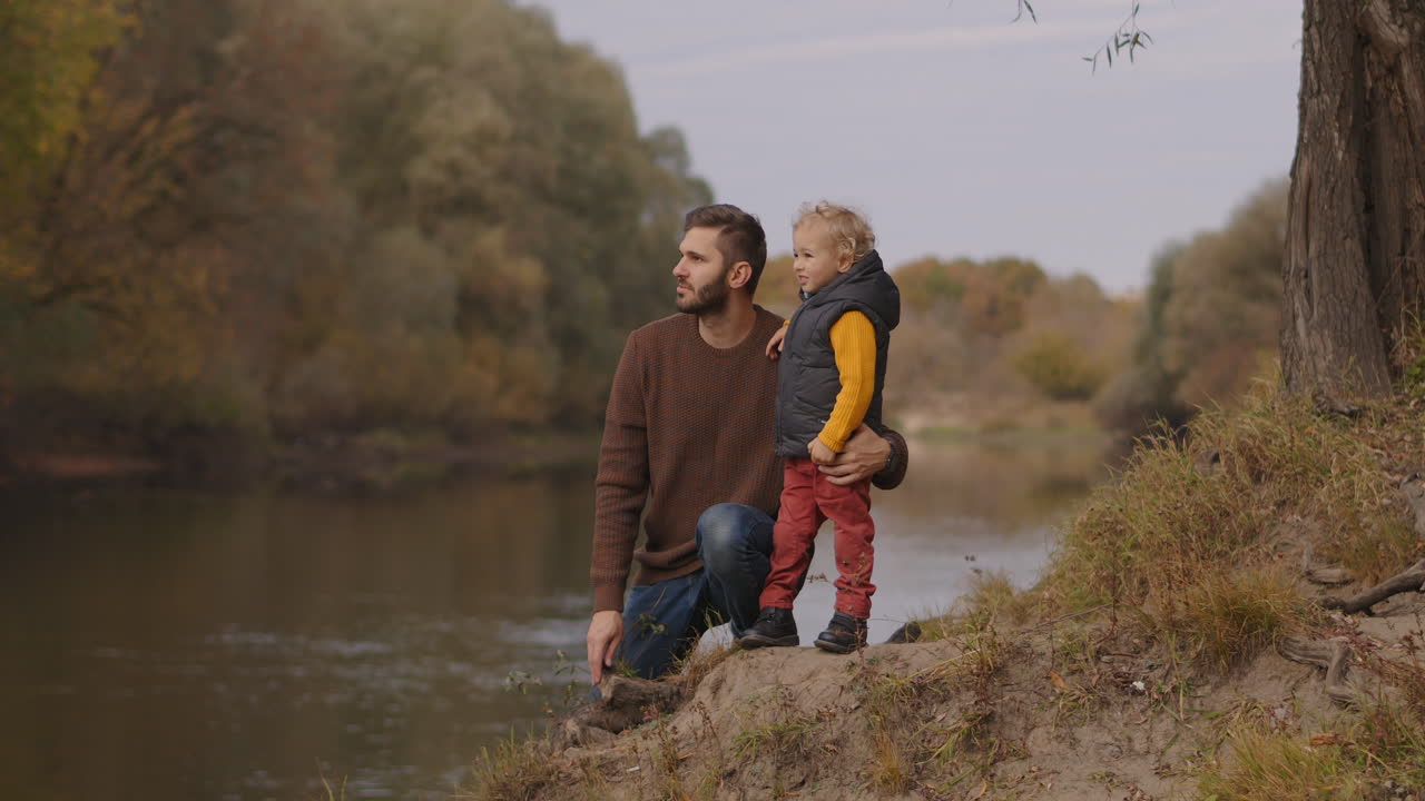 bambino gioioso è in piedi vicino al padre sulla riva del fiume in autunno foresta relazioni familiari felici trascorrere il fine settimana insieme riposare in natura