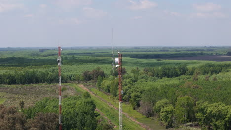 tall communication tower stands in a rural landscape, surrounded by greenery and open fields, aerial approach