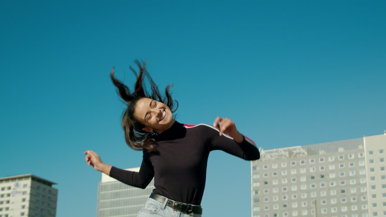 권한이 부여 된 행복하고 매력적인 젊은 라틴 여성은 춤을 추고 머리를 움직이고 도시에서 화창한 날 점프를 즐깁니다.