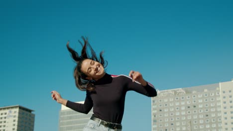 Empoderada,-Feliz,-Joven-Y-Atractiva-Mujer-Latina-Disfruta-Bailando-Y-Moviendo-Su-Cabello-Y-Saltando-En-Un-Día-Soleado-En-La-Ciudad