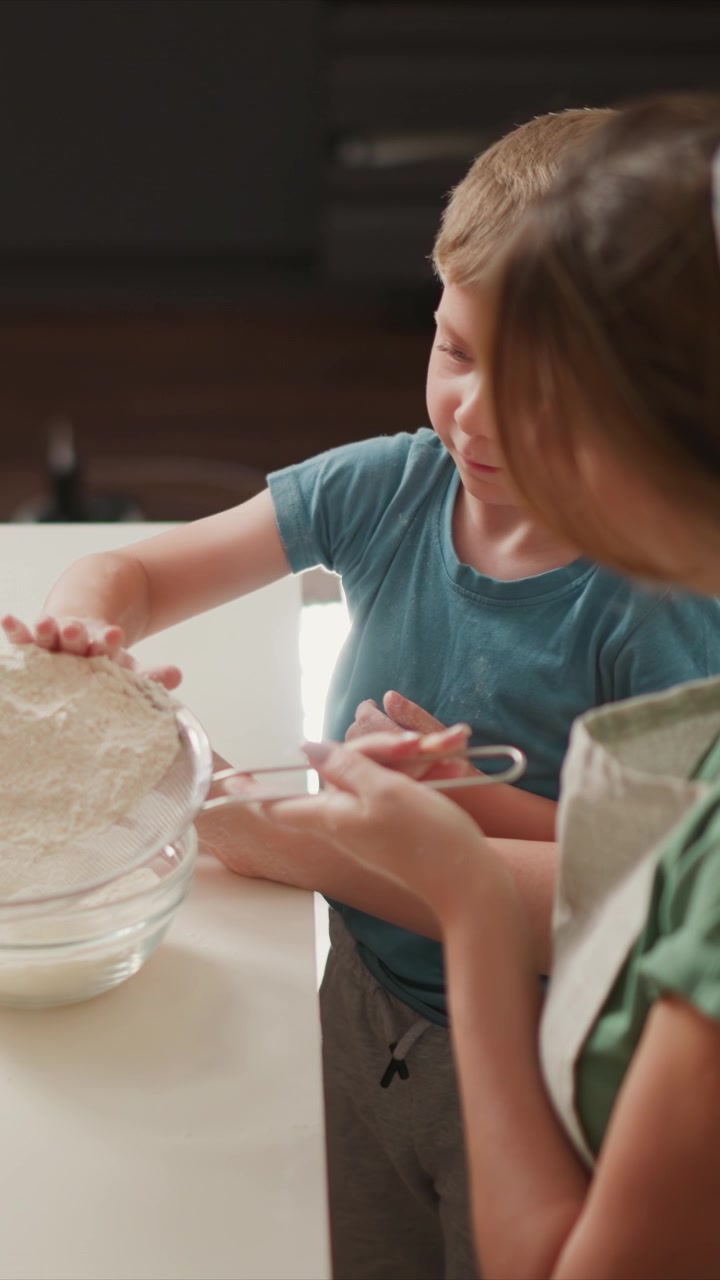 Young boy and woman work together in kitchen sifting flour into bowl. child actively participates while adult assists with baking preparation on clean countertop