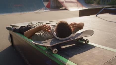 young boy lying on skateboard listening to music with headphones