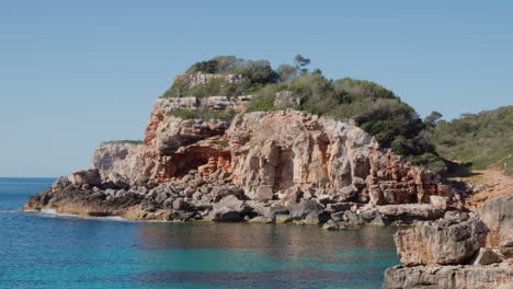 Turquoise-waters-encircled-by-rock-formations-and-green-plants-in-Mallorca,-Spain,-creating-a-serene-scene-of-natural-beauty