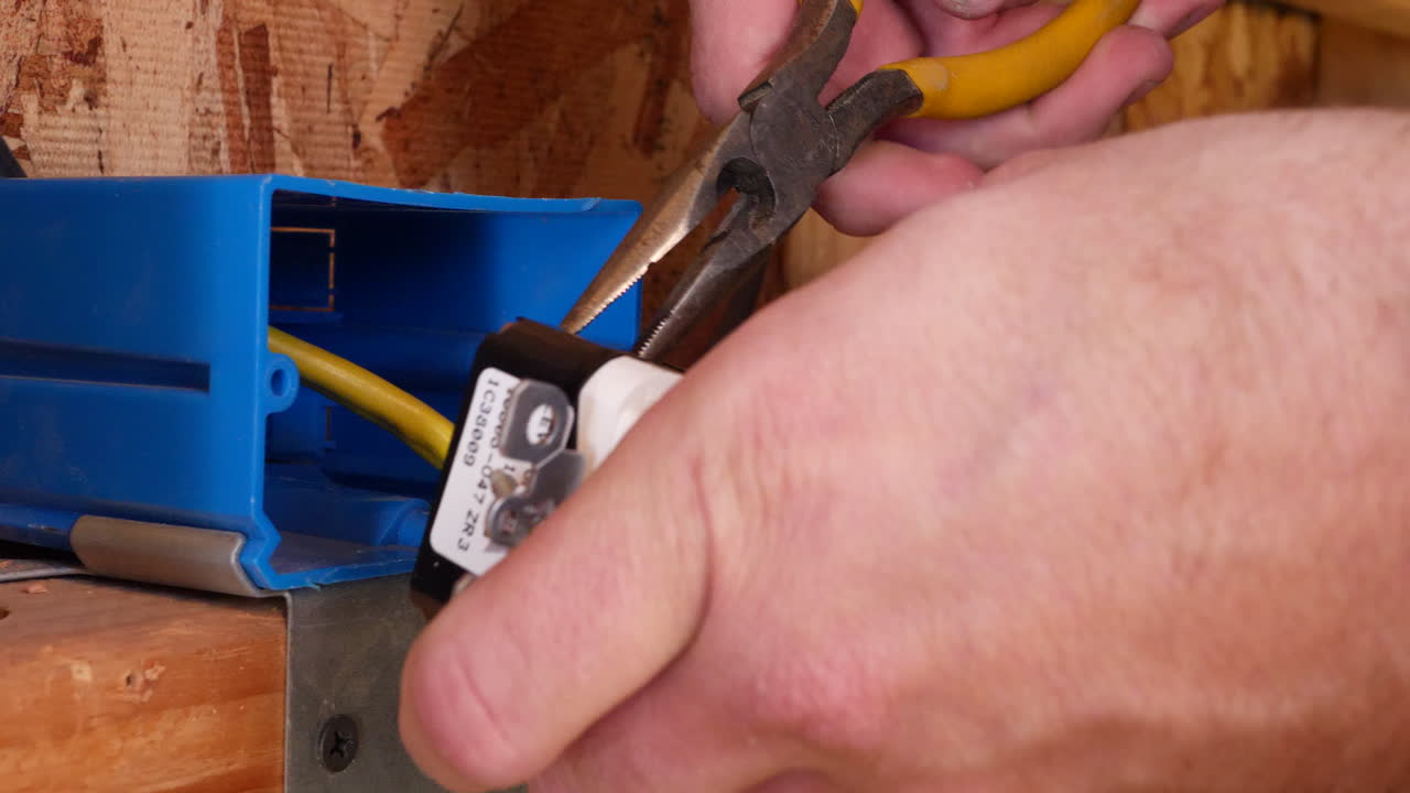 A construction worker using pliers to install an electrical outlet with wires in the framing of a new home