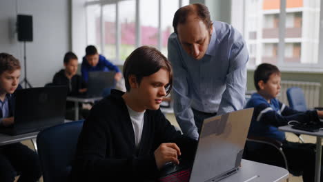 maestro ayudando a los estudiantes con computadoras portátiles en un aula