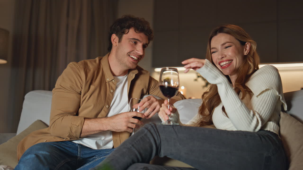 Happy couple spending evening together at home couch holding wineglasses closeup