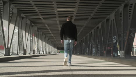 Young-European-Male-with-Black-Jacket,-White-Sneakers-and-Jeans-and-Man-Bun-walking-in-the-middle-of-Empty-Street-in-Hamburg,-Germany