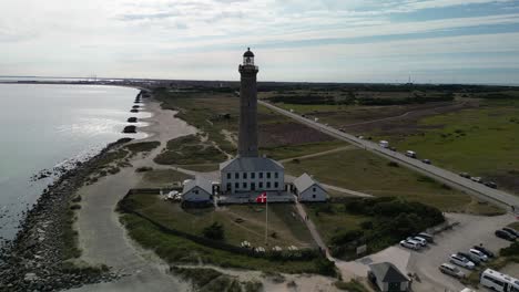 Aerial-Orbit-of-Skagen-Lighthouse-with-Danish-Flag,-Skagen,-Denmark