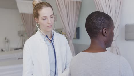 diverse female patient and doctor, using stethoscope on her back in hospital, in slow motion