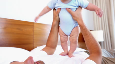 padre feliz acostado con el bebé hijo rebotando en su pecho