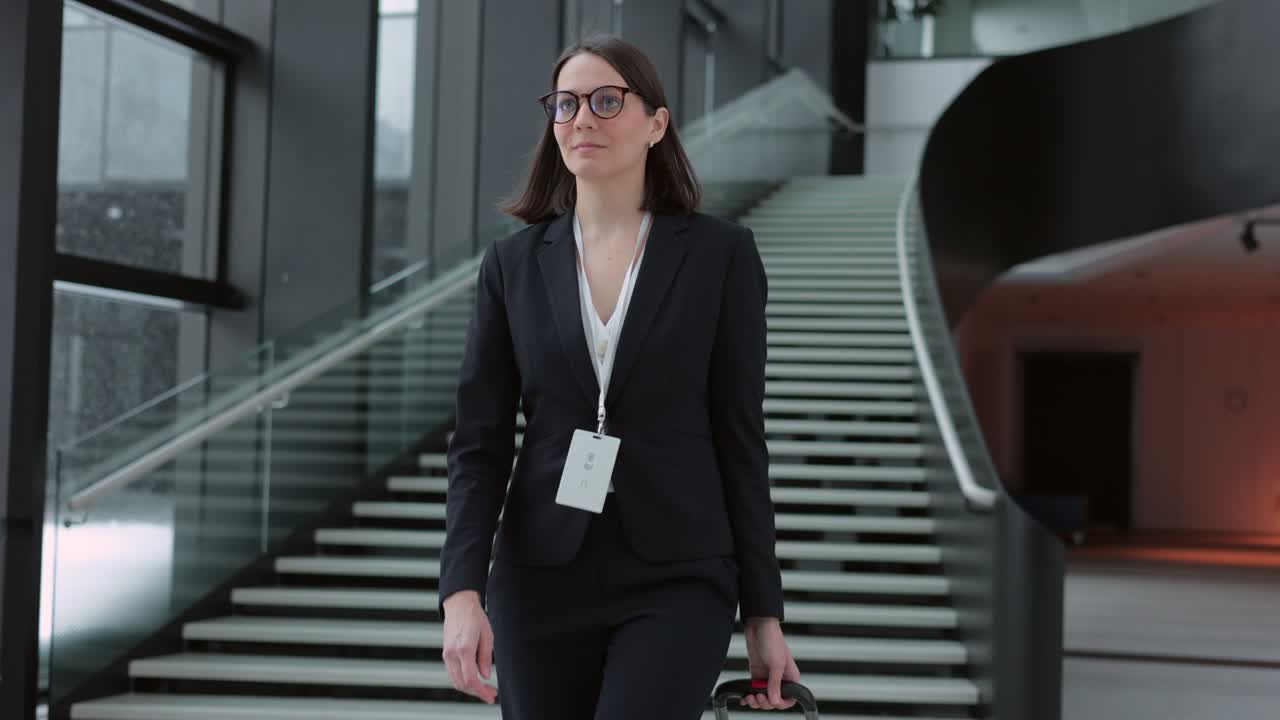 mujer de negocios con un traje de negocios con una maleta camina por el aeropuerto o el centro de negocios y habla por teléfono. una mujer europea confiada