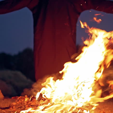 fire explodes on the ground before silhouette of death. black robe waving arms near the bright flame in the evening. horror ghost at night.