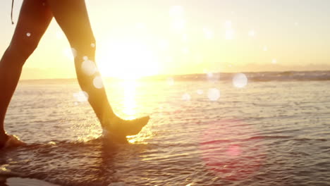 woman walking barefoot in ocean on the sand against sunshine on ocean