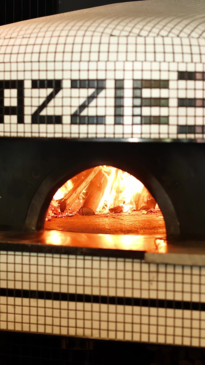 Inquadratura media statica di un tradizionale forno per pizza piastrellato con fiamme arancioni brillanti che bruciano all'interno.