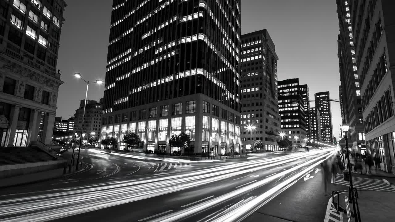 Black and white cityscape at night with tall buildings and light trails