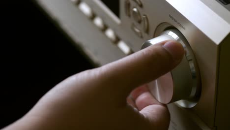 men's hands adjusting volume control of the amplifier form the home theater system with the adjust button for broadcasting and music