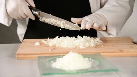 selective focus and close up of a chef wearing gloves chopping onion on a cutting board and cleaning the knife. cooking and safety concept.