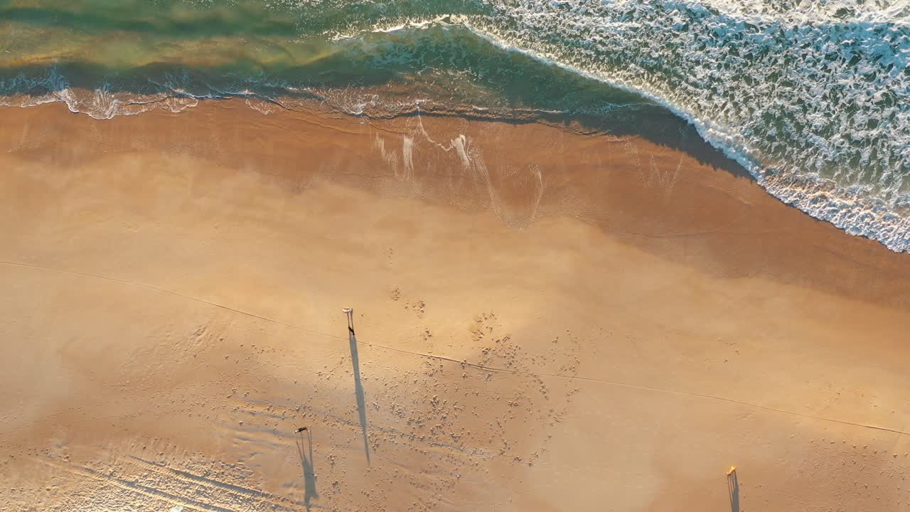 Beach sunrise shining golden foamy waves rolling towards sand top down view going up