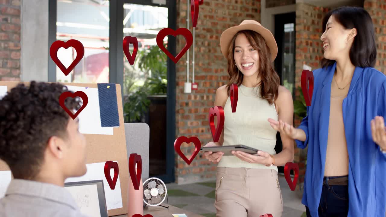 Two women pitching design moodboard tapping tablet making floating red hearts around people smiling