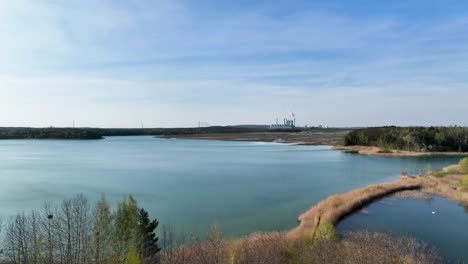 Imágenes-Aéreas-De-Reserva-Natural-Con-Bosque-De-árboles-Y-Agua-De-Laguna-Azul-Con-Planta-De-Energía-De-Carbón-Industrial-A-Distancia