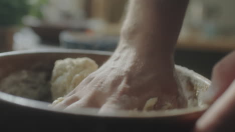 hands kneading dough in wooden bowl