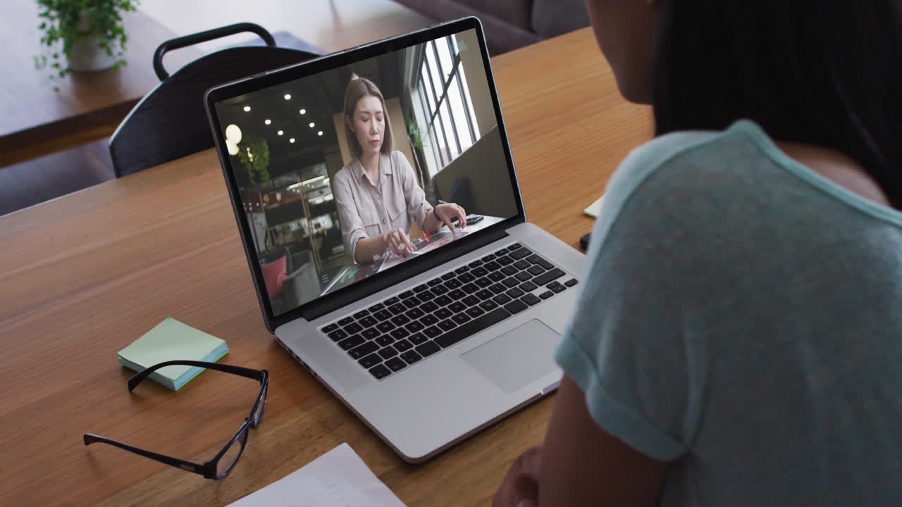 Biracial businesswoman sitting at desk using laptop having video call with female colleague