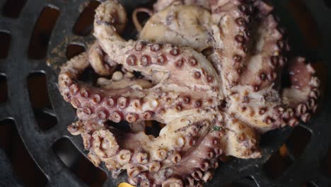 toma giratoria de arriba hacia abajo cinematográfica de un pulpo que se cocina sobre una parrilla de barbacoa de llama abierta con fuego ardiente que captura todos los detalles finos de las ventosas en los tentáculos del pulpo