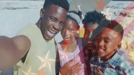 animación de la bandera de américa sobre un hombre afroamericano tomando una selfie con su familia en la playa